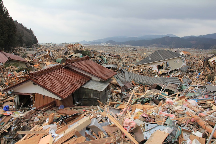 Two homes surrounded by rubble as far as the eye can see.