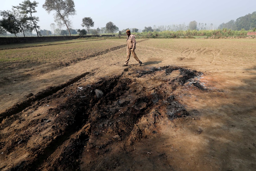 A police officer walks next to a charred spot in the ground.