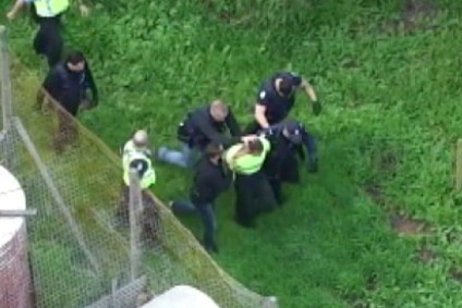 An aerial shot showing police officers escorting a man away in handcuffs.