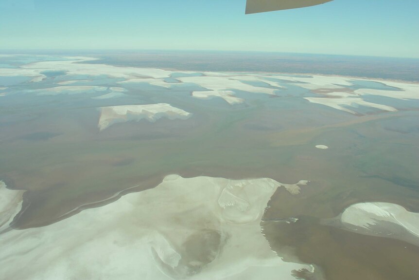 A aerial shot of a large salt pan. There is a plane wing in the shot.
