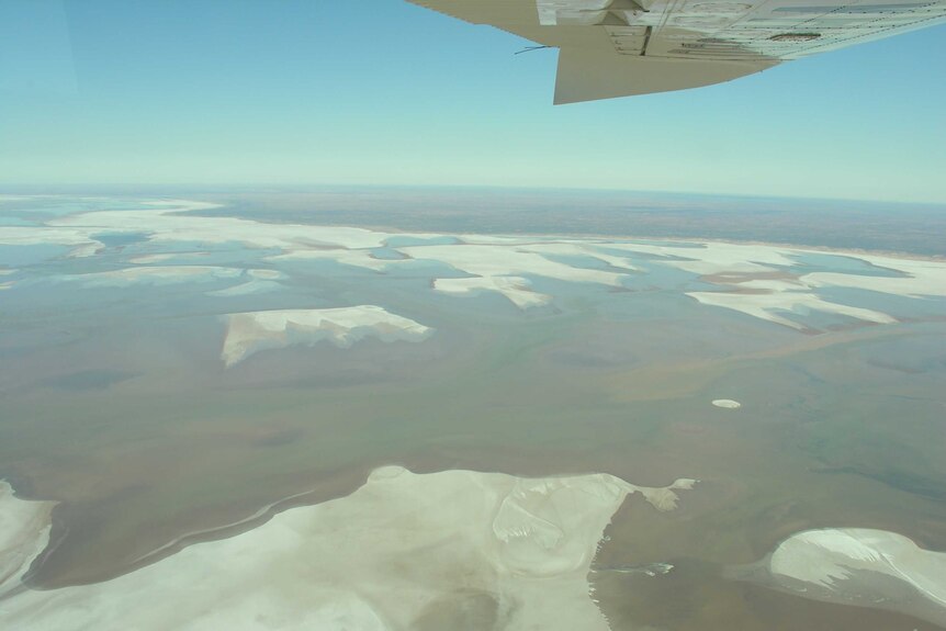 A aerial shot of a large salt pan. There is a plane wing in the shot.