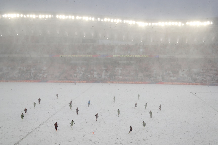 A soccer game takes place in heavy white snow inside a stadium in North America