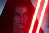 A woman's face is lit with red light from two lightsaber blades.