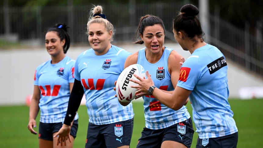 Two women in blue exchange a rugby ball while two teammates behind them look on
