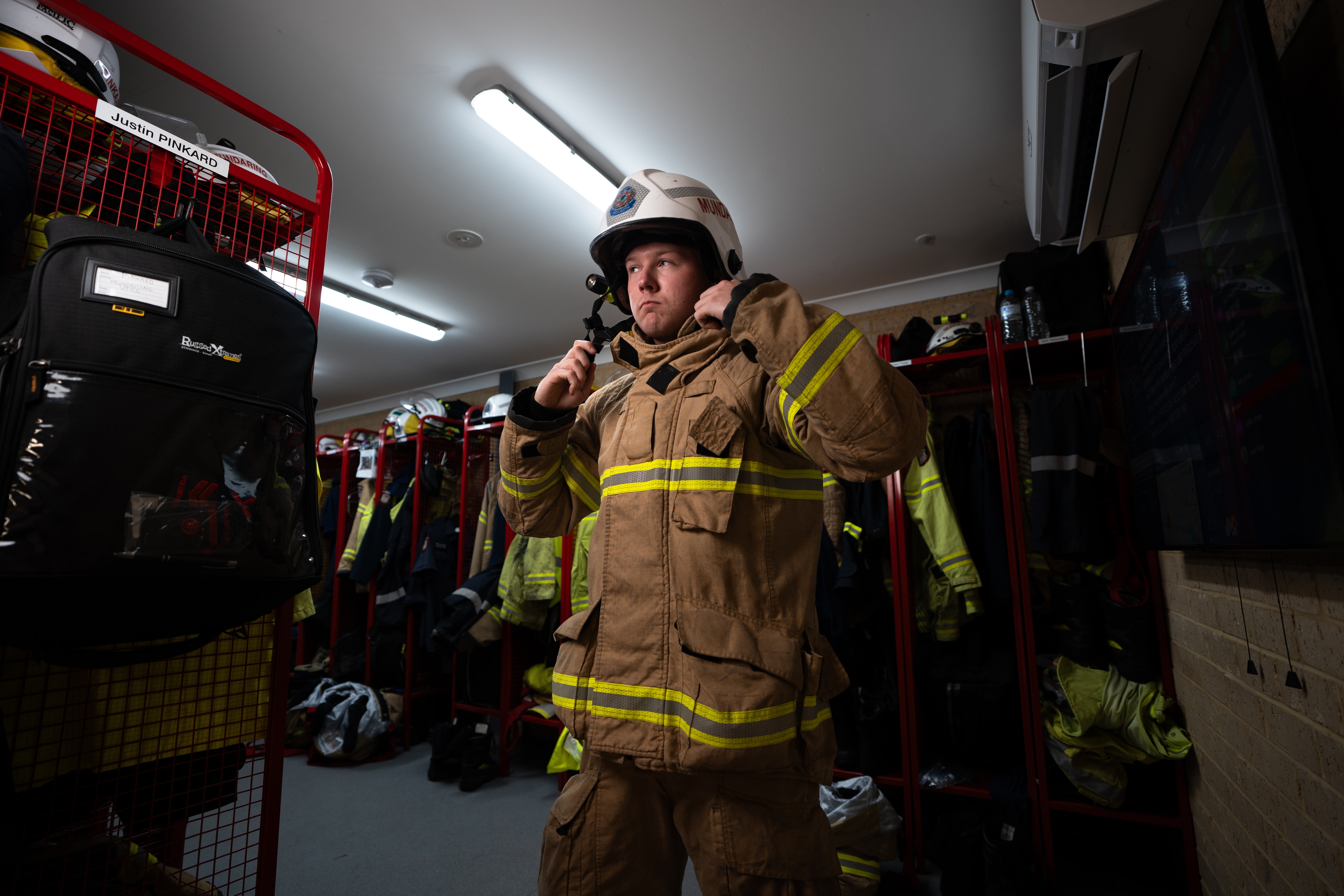 Imagen cambiante y con iluminación lateral de un hombre parado en una estación de bomberos con poca luz.