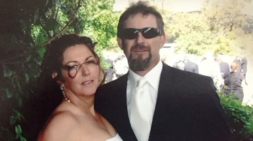 A man and a woman at their wedding. She is in a white wedding dress, he is in a wedding suit with sunglasses.