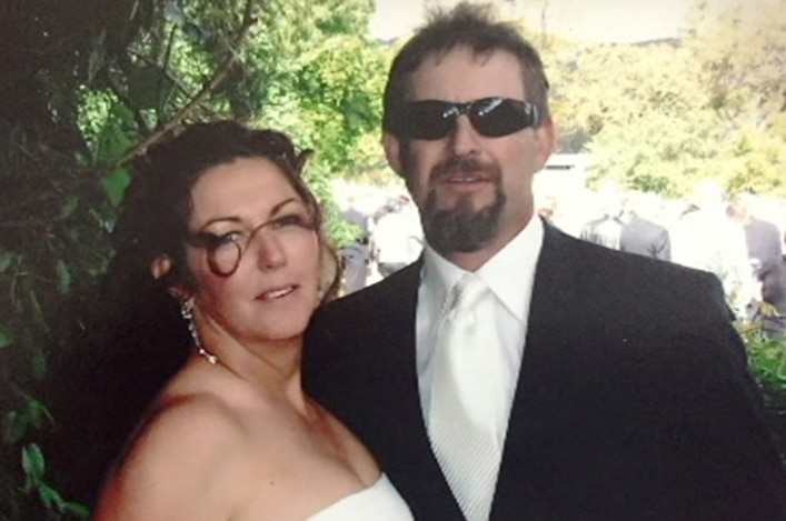 A man and a woman at their wedding. She is in a white wedding dress, he is in a wedding suit with sunglasses.
