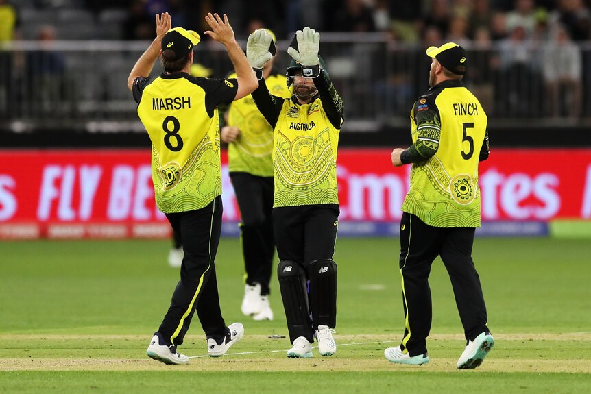 A group of men in green and gold Australian T20 cricket uniforms high-five in the middle of the pitch.