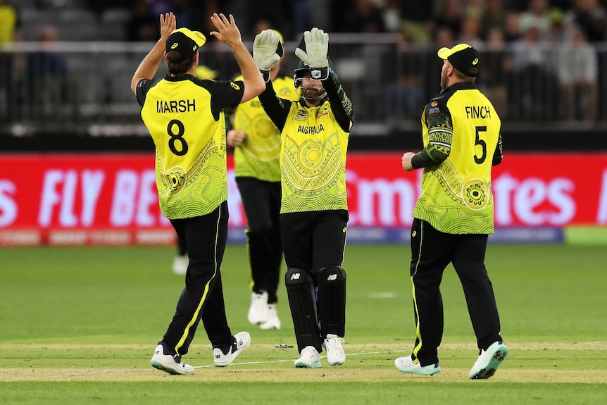 A group of men in green and gold Australian T20 cricket uniforms high-five in the middle of the pitch.