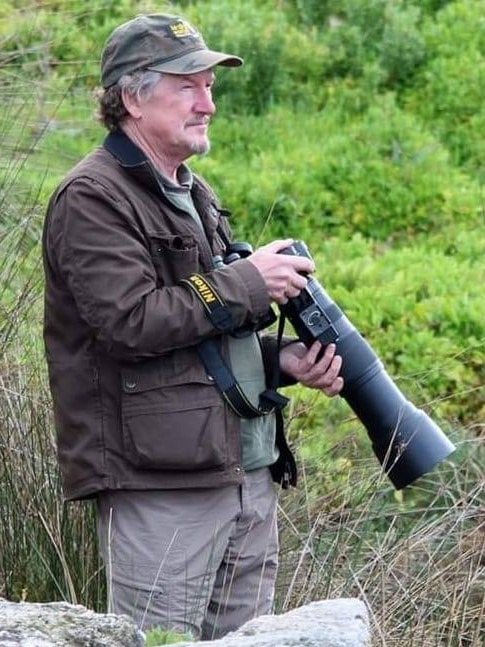 A man, holding a big camera, looks for birds