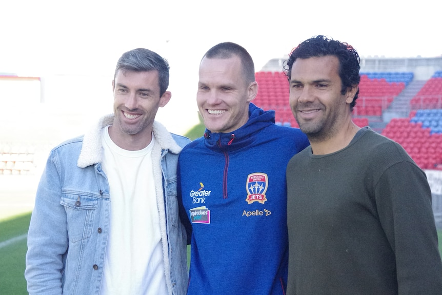 Three soccer players stand smiling.