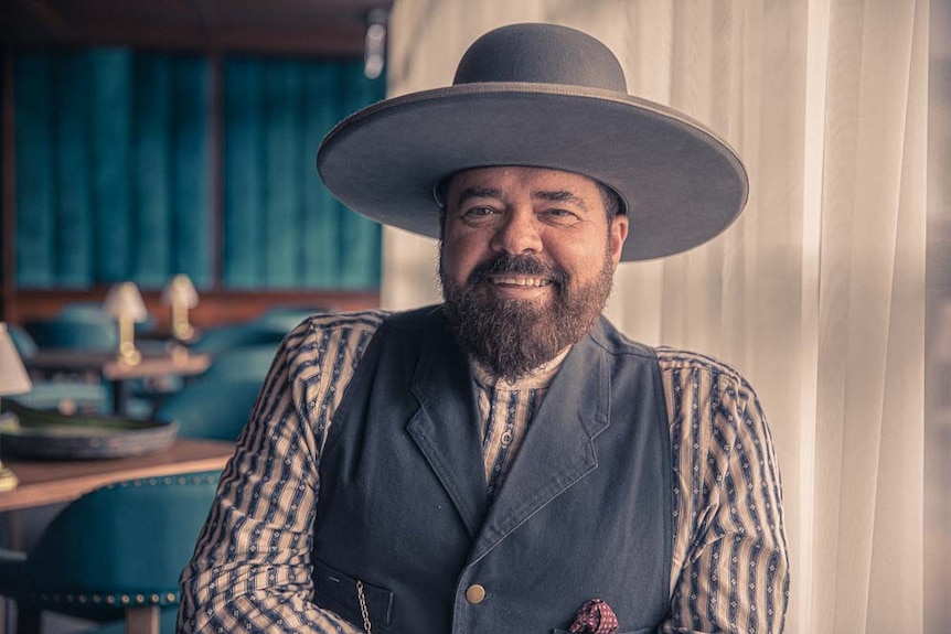 Ex-INXS band member sits in a hotel bar dressed in country attire and a ten-gallon hat.