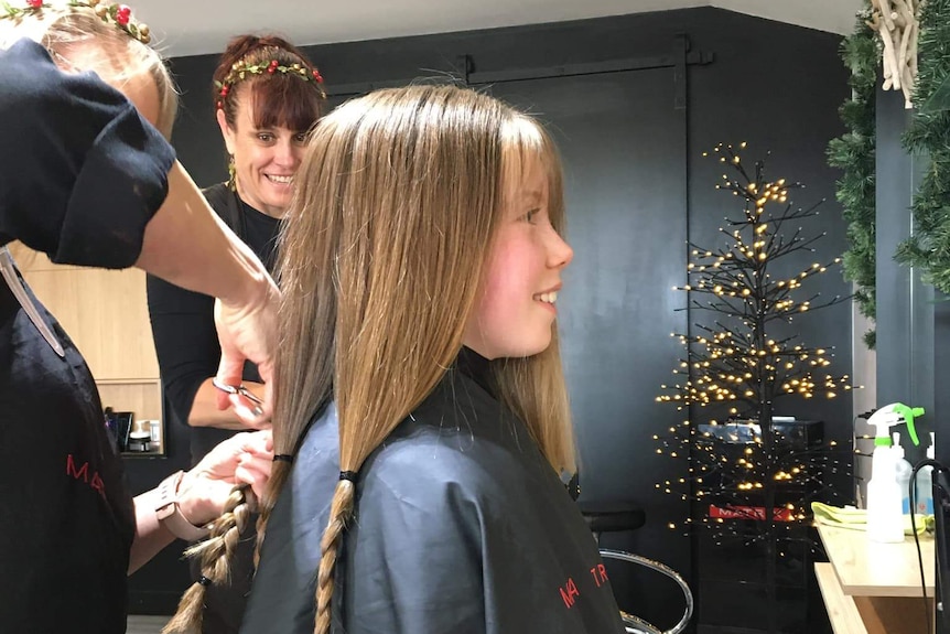 A girl setting in a hair salon seat getting a haircut.