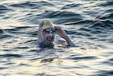 Sarah Thomas smiles while lifting her goggles off her face. She is in deep water and has white paint smeared on her skin.
