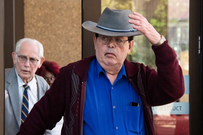 A man leaves court wearing a hat