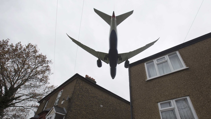 A plane flies over houses.