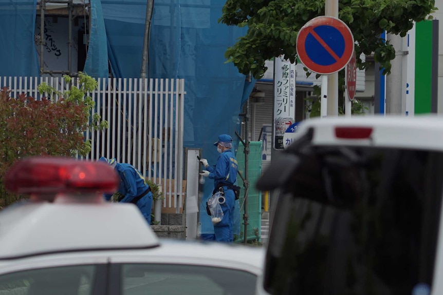 A man in a blue jumpsuit scrapes something off a post