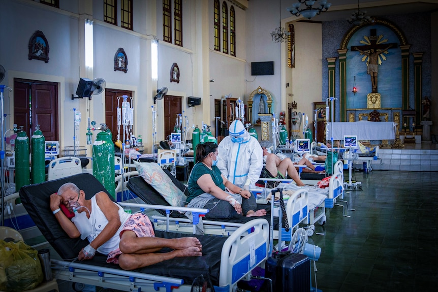 Un'infermiera in DPI parla con una donna in un letto d'ospedale allestito in un reparto improvvisato in una cappella