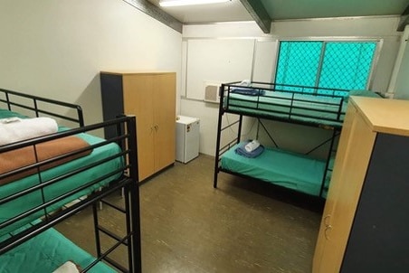 Four bunk beds in a fairly spartan room with a bar fridge and two cupboards.