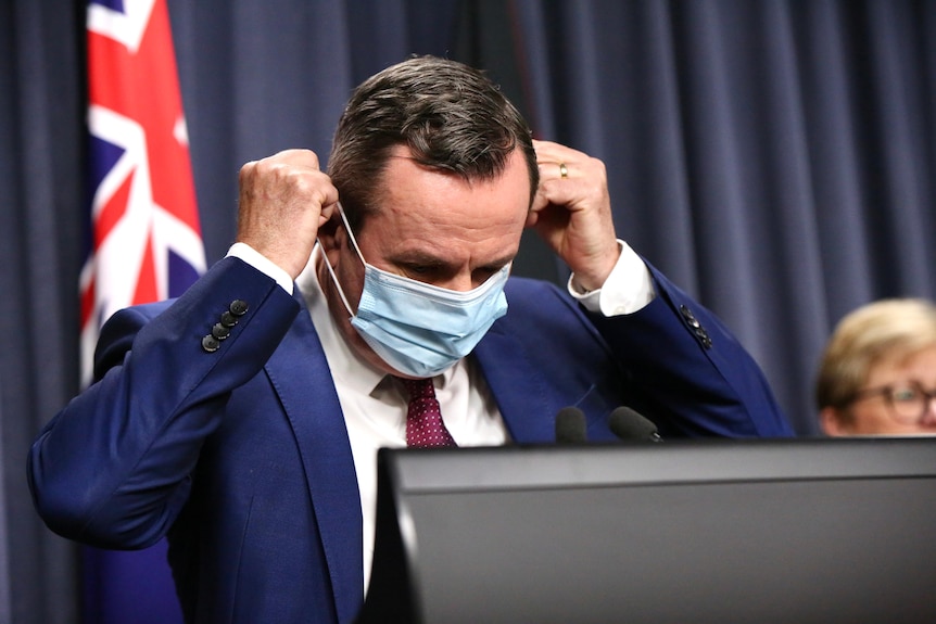 Mark McGowan removes his mask before speaking at a press conference.