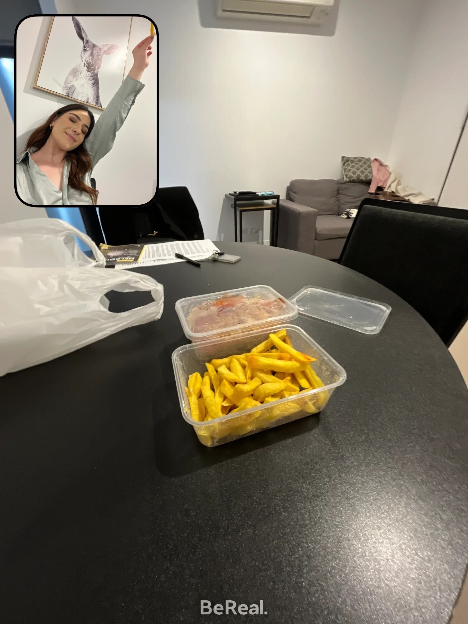 Screenshot of BeReal app, showing a room with takeaway food containers on a table, embedded with a selfie of a young woman