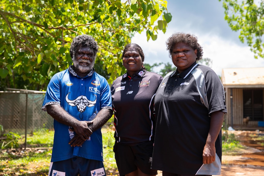 A young woman stands between her parents as all three look towards the camera