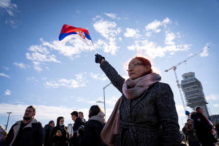 A supporter of Novak Djokovic holds a Serbian flag above her head at Belgrade airport