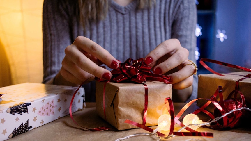 A woman with red nail polish wraps up and decorates a gift. Her face is not visible.