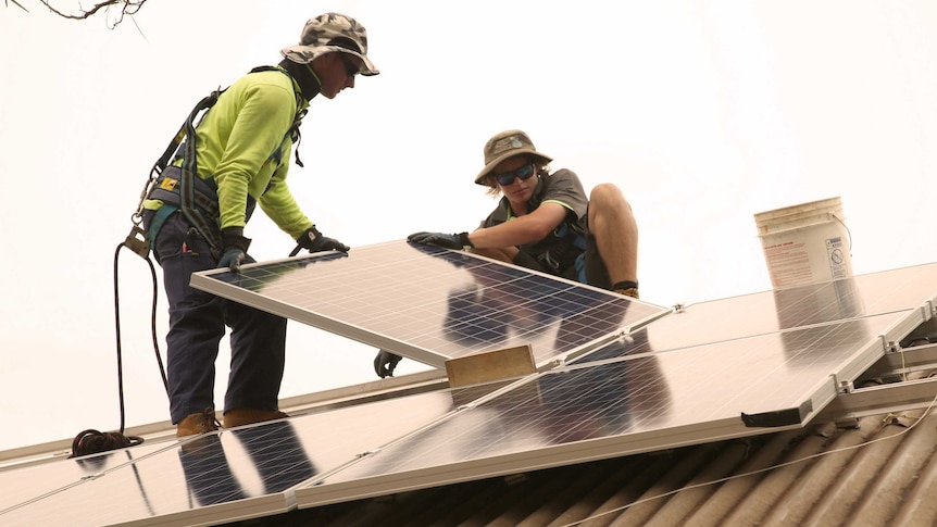 Electricians Lochie Barclay (r) and Jayde Ralph installing solar panels on a house in Broome.
