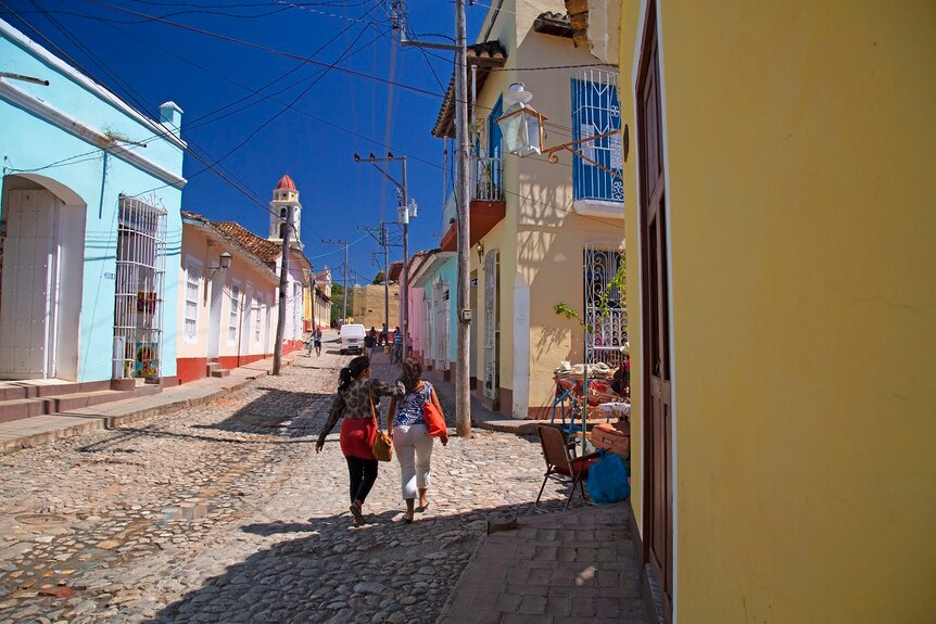 Two women walk down a cobbled street surrounded by colourful colonial buildings.