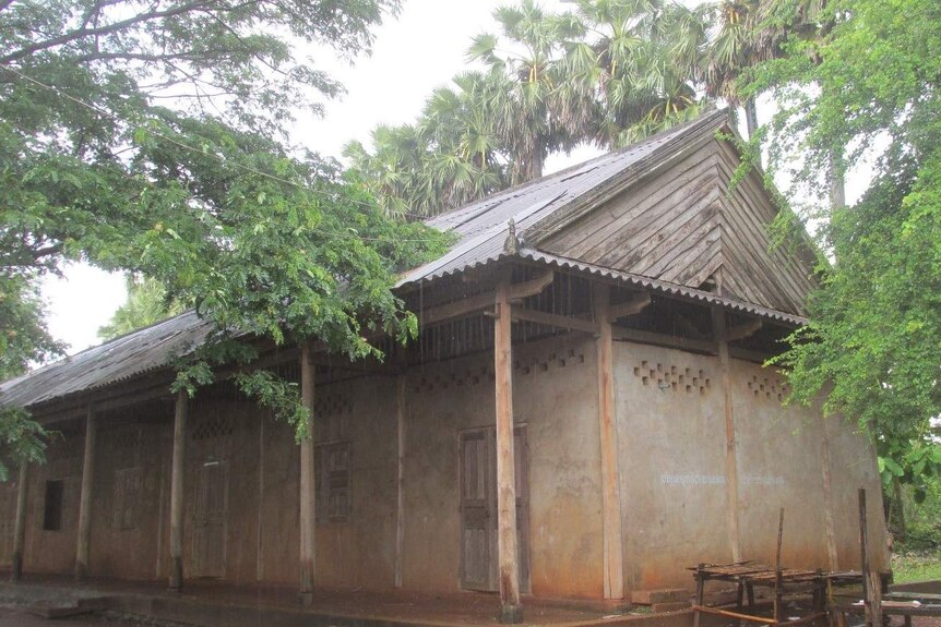 A building made of brick and wood with patched roof stands among trees