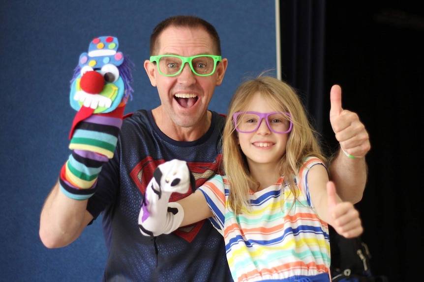 A man in kooky glasses and a little girl wearing similar glasses hold up sock puppets and give the thumbs up sign