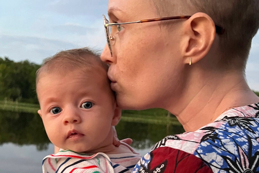 A woman with shaved hair kisses a baby 