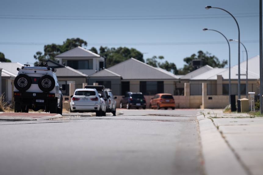 A treeless street with parked cars under a blazing sun in suburban Perth.