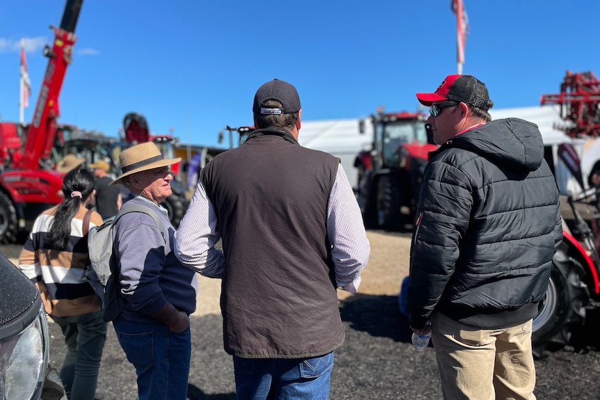 Three men stand with their backs to the camera, looking at red tractors.