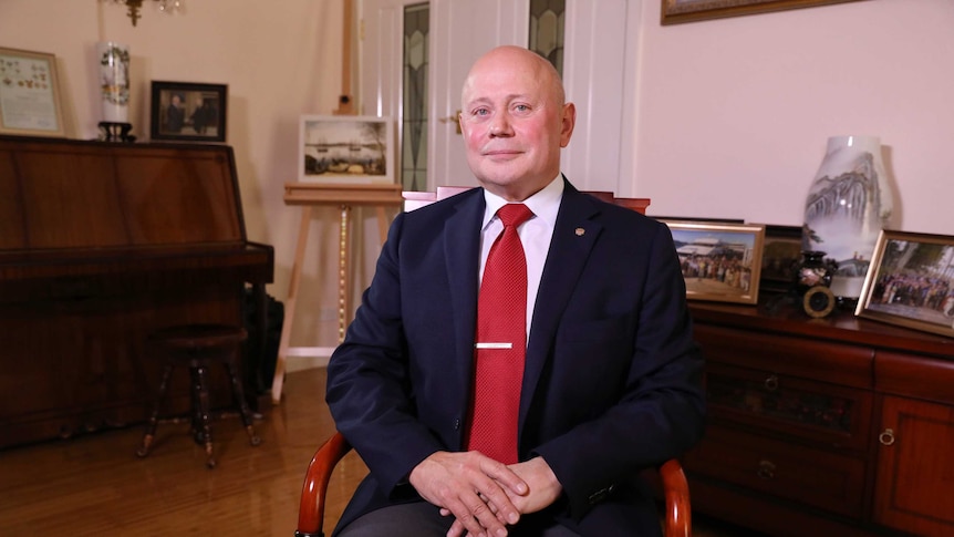 Logvinov, wearing a suit, sits in a chair with his hands folded