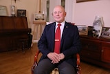 Logvinov, wearing a suit, sits in a chair with his hands folded