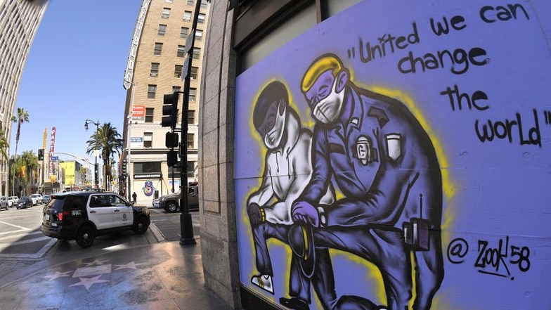 Mural on city street shows black man and white police officer, both wearing masks, with words: United we can change the world