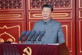 Xi Jinping delivers a speech in front of red doors and a podium with a sickle and hammer.