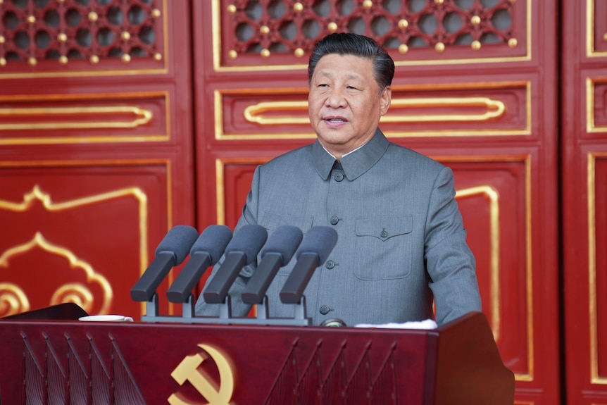 Xi Jinping prononce un discours devant des portes rouges et un podium avec une faucille et un marteau.
