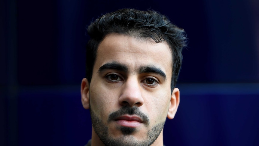 A portrait of a man looking serious towards the camera. He has a short beard and moustache