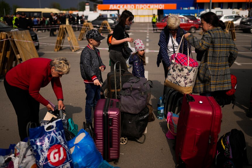 People with luggage stand in a car park outside a reception centre for displaced people.