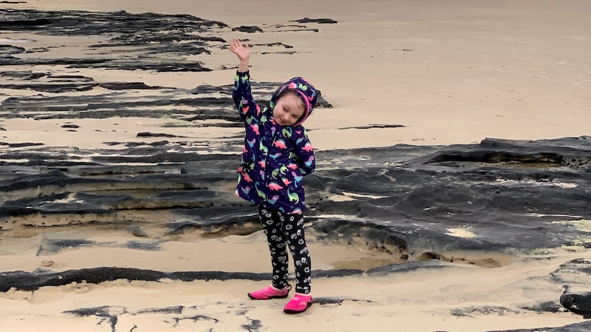 A young girl in a raincoat with the beach in the background.