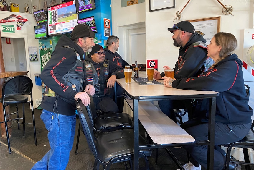 six people in motorcycle gear sit around a table and talk.