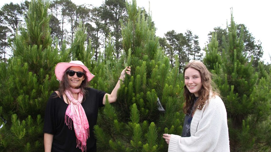 Woman and her teenage child smile next to their pick of all the Christmas trees