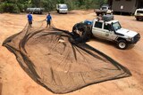 A photo of a very large ghost net splayed out on sand.