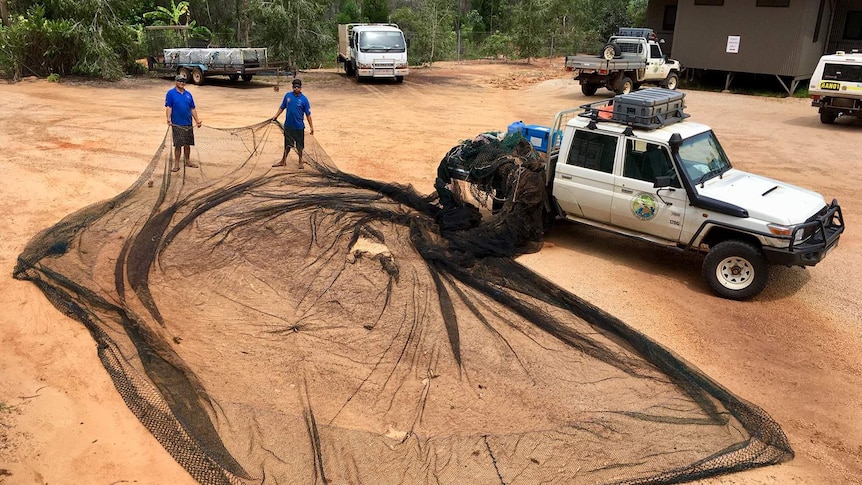 A photo of a very large ghost net splayed out on sand.