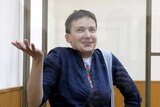 Nadezhda Savchenko gestures from inside a glass-walled cage in court.