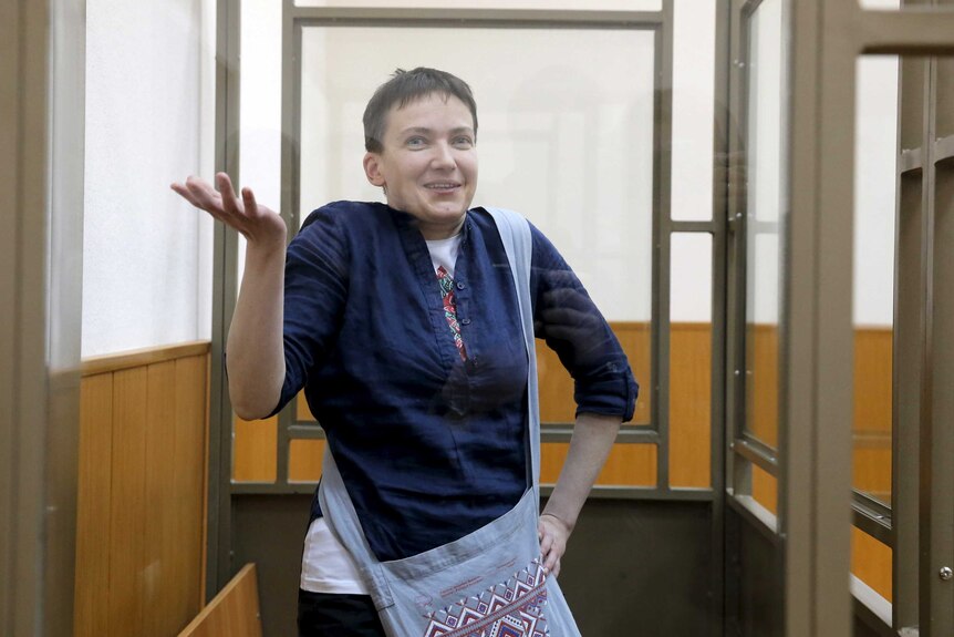 Nadezhda Savchenko gestures from inside a glass-walled cage in court.