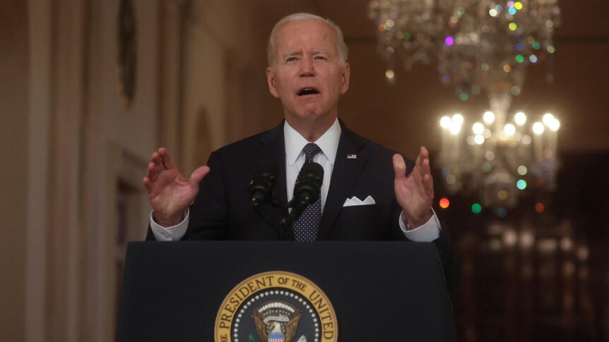 US President Joe Biden speaking at a lecturn with the presidential seal on it, wearing a suit and gesturing